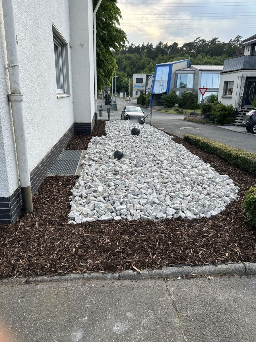 Nachher: fertiges Beet mit Rindenmulch, weißem Zierkies und Kugeln